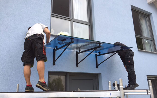 Zwei Männer befestigen Glasvordach