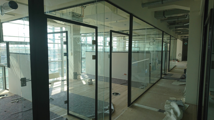 Modern Bürofläche mit Glaswänden, offenen Türen und Baustellenmaterialien am Boden