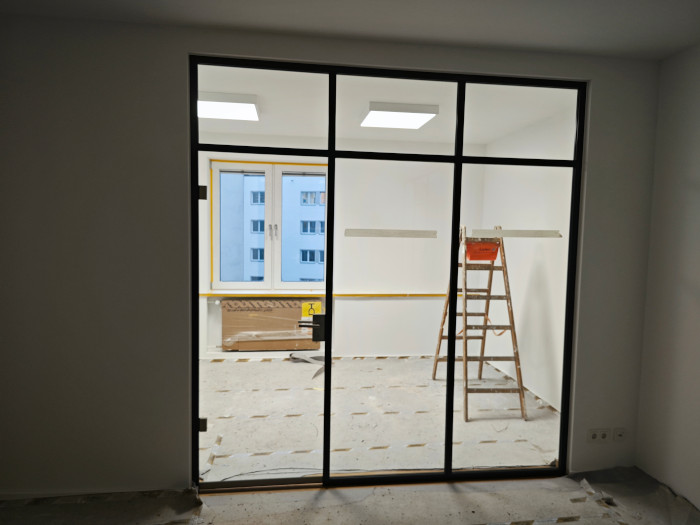 Ein leerer heller Raum mit Leiter, großen Fenstern und sichtbaren Baustellenmaterialien
